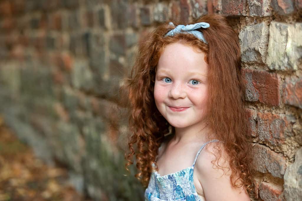 family photoshoot, girl with red hair by brick wall